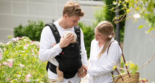 Eltern streicheln ihr Baby in der manduca Babytrage und lächeln